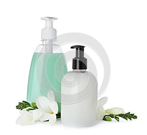 Dispensers of liquid soap and freesia flowers on white background