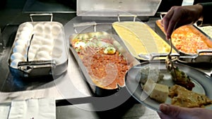 Display of food at an evening buffet at a tourist hotel. Woman puts meal on her plate