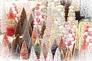 Display of pastel and brown bottle brush and pompom Christmas trees with glitter and lots of pink