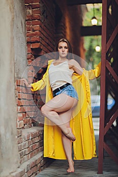 Displaying fashion tendencies. Dark-haired attractive woman posturing in bright yellow fluffy cloak.