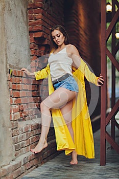 Displaying fashion tendencies. Dark-haired attractive woman posturing in bright yellow fluffy cloak.