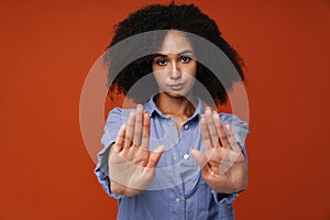 Displeased african woman making stop gesture and showing palms isolated over red wall