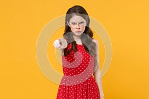 Displeased angry young brunette woman girl in red summer dress posing isolated on yellow wall background studio portrait