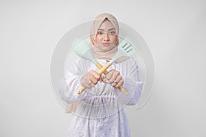 Displeased Asian woman in veil hijab doing a refusal or rejection sign, saying no, asking to stop gesture using spatula and