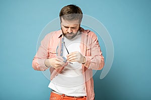 Displeased bearded man cleans his glasses from dust and dirt, wiping them with a shirt.  on a blue background.