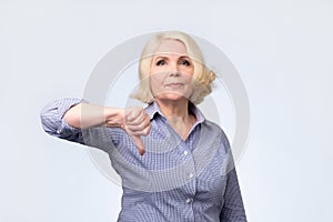 Displeased blonde senior woman showing thumb down