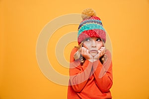 Displeased girl in sweater and hat reclines on her arms