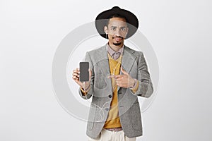 Displeased guy showing disgusting thing in smartphone. Portrait of disappointed good-looking stylish man in black hat