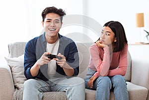 Displeased Japanese Girlfriend Looking At Boyfriend Playing Game At Home