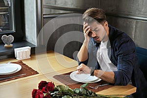 Displeased man looking at watch while waiting for his girlfriend in restaurant