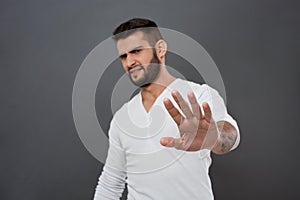 Displeased man refusing, stretching hand to camera over grey background.