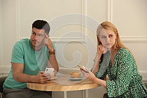 Displeased man and woman with smartphones in cafe. Failed first date