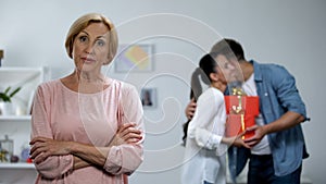 Displeased mother-in-law looking her son presenting gifts to wife, jealousy