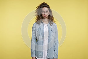 Displeased pretty brunette woman makes a funny disappointing face , isolated over yellow background