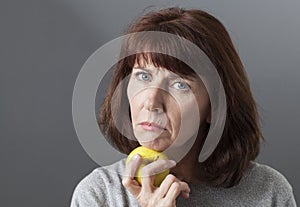 Displeased 50s woman thinking about skin aging with symbol of healthy lifestyle and fresh food in hand