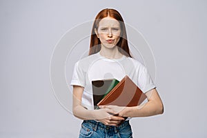 Displeased sad young woman college student holding book and looking at camera on gray background