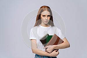 Displeased sad young woman college student holding book and looking at camera on gray background