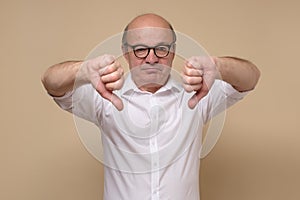 Displeased senior man in white shirt giving thumb down