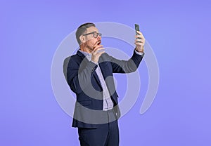 Displeased shocked young businessman dressed in suit reading messages on mobile phone. Worried male professional entrepreneur