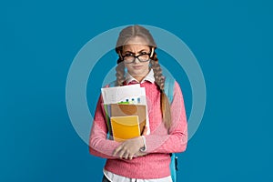 Displeased teenager girl with glasses on nose, looks disapprovingly and holds notebooks