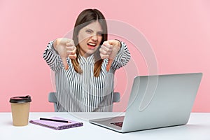 Displeased woman office worker showing thumbs down, dislike gesture, expressing disapproval, criticizing sitting at workplace with