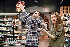 Displeased woman showing at man with keg of beer
