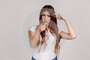 Displeased woman showing stupid gesture and pointing to camera, accusing of dumb idea.