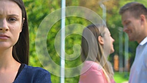 Displeased woman standing against happy couple of best friend and ex-boyfriend