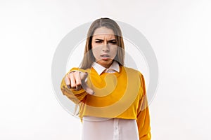 Displeased young brunette woman is pointing finger at camera, angry and furious with you. Studio shot, white background
