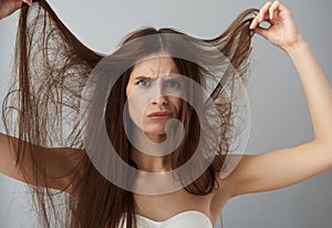 Displeased young lady in white bra demonstrating her damaged hair