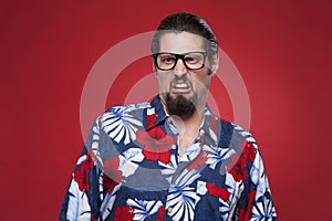 Displeased young man in Hawaiian shirt against red background