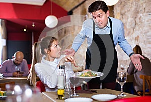 Displeased young woman conflicting with apologetic waiter because of poor quality of dish