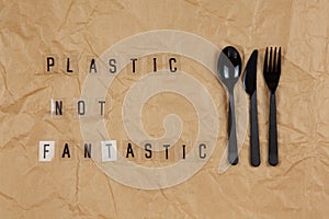 Disposable black appliances fork, spoon, knife, phrase from letters on transparent base Plastic not fantastic on brown crumpled