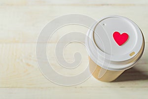 Disposable craft paper coffee cup and red wooden heart on a cap. Coff to go on wooden table
