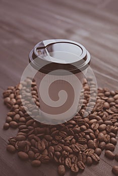 Disposable cup of coffee and coffee beans over dark wood background with space for your text