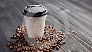 Disposable cup of coffee and coffee beans over dark wood background with space for your text