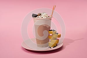 Disposable cup of milkshake with drinking straw, cut banana and chocolate chips on plate