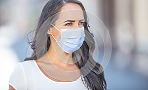 Disposable face mask on a face of young dark-haired female looking to the side