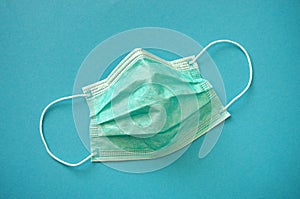 Disposable face mask. Green blue medical respirator breathing face dust mask on blue background. Coronavirus Covid-19 prevention.