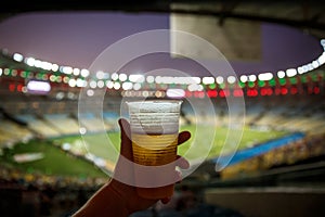 Disposable glass with beer. Soccer stadium on the background