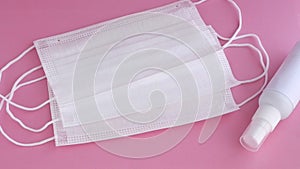 Disposable masks, earloop type, with spray alcohol bottle on soft pink surface, slowly movement