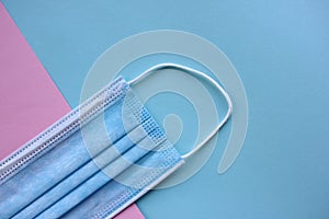 Disposable medical face mask on blue and pink background with copy space. Pandemic protective face cover.