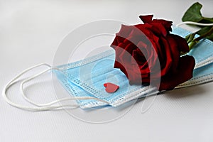 Disposable medical face mask with red heart and red rose on white background. Safe Valentine`s Day during the coronavirus pandemi