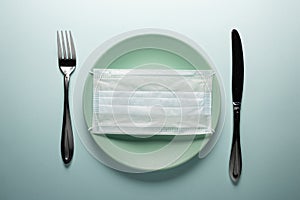 Disposable medical mask on a round plate with a knife and fork. Concept photo