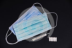 Disposable mouth masks with a mercury clinical thermometer and 5 tablets on a slate plate.