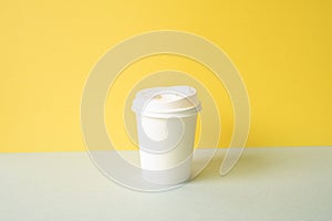 Disposable paper coffee cup on gray table. yellow wall background