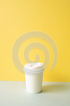 Disposable paper coffee cup on gray table. yellow wall background