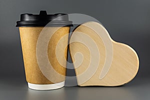 Disposable paper Cup for coffee or tea. A large wooden heart and coffee on a gray background. Coffee to go