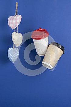 disposable paper flying coffee cups with textile hearts on a blue background hanging on. Takeaway coffee concept. I love coffee