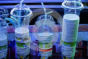 Disposable paper glasses and cups with lid and straw stacked one another.